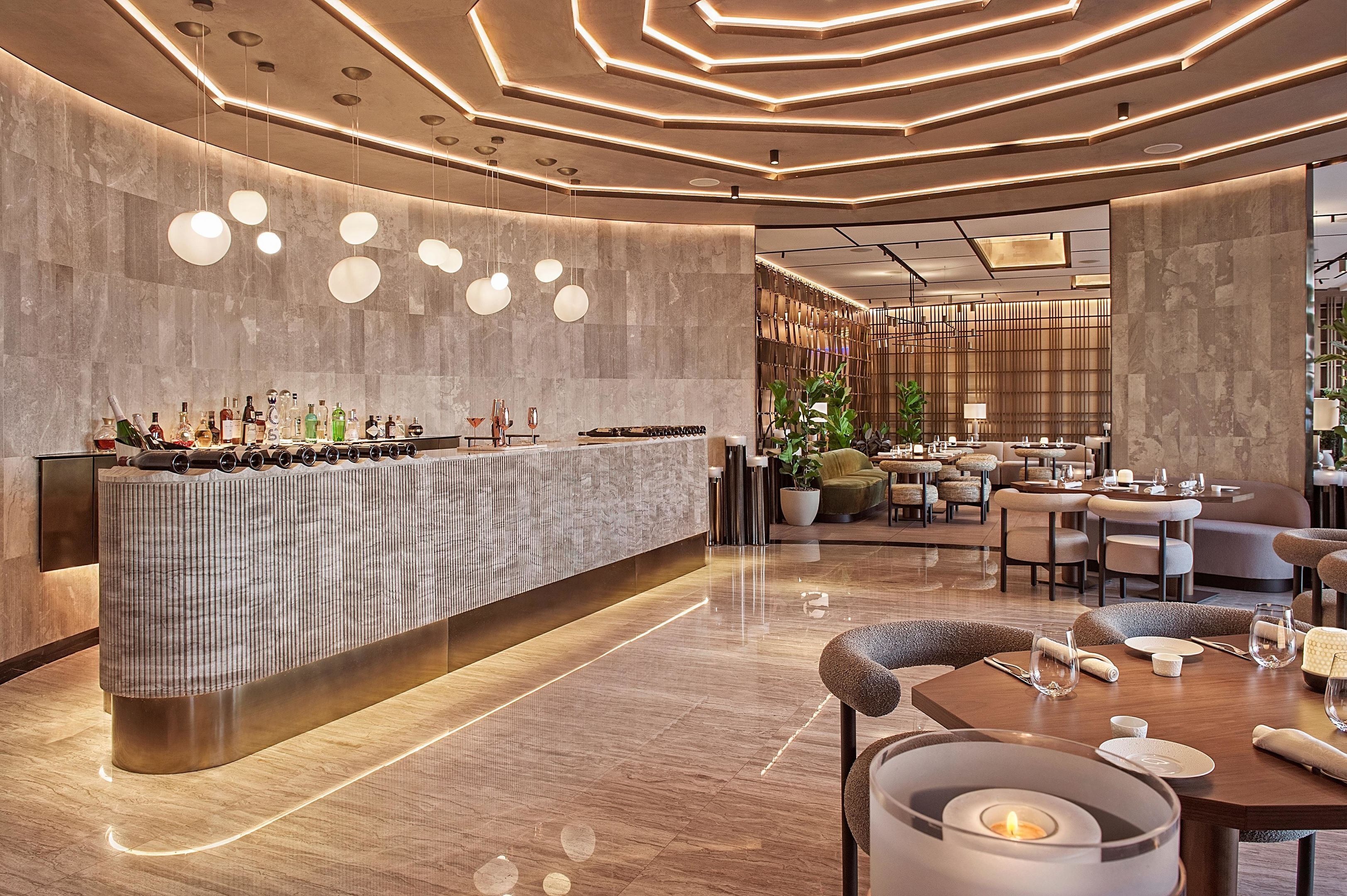 A modern hotel lobby with a reception desk, seating area, and a bar.