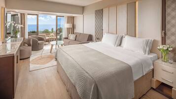 A modern hotel room with a large bed, a sitting area with a glass table, and a view of the ocean.