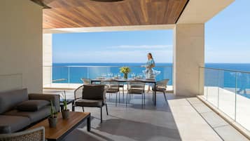 A modern outdoor dining area with a view of the sea, featuring a wooden ceiling, a table set for dining, and comfortable seating.
