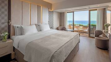 Une chambre d’hôtel dotée d’un grand lit, d’un coin salon avec vue sur la mer et d’un balcon avec une table et des chaises.