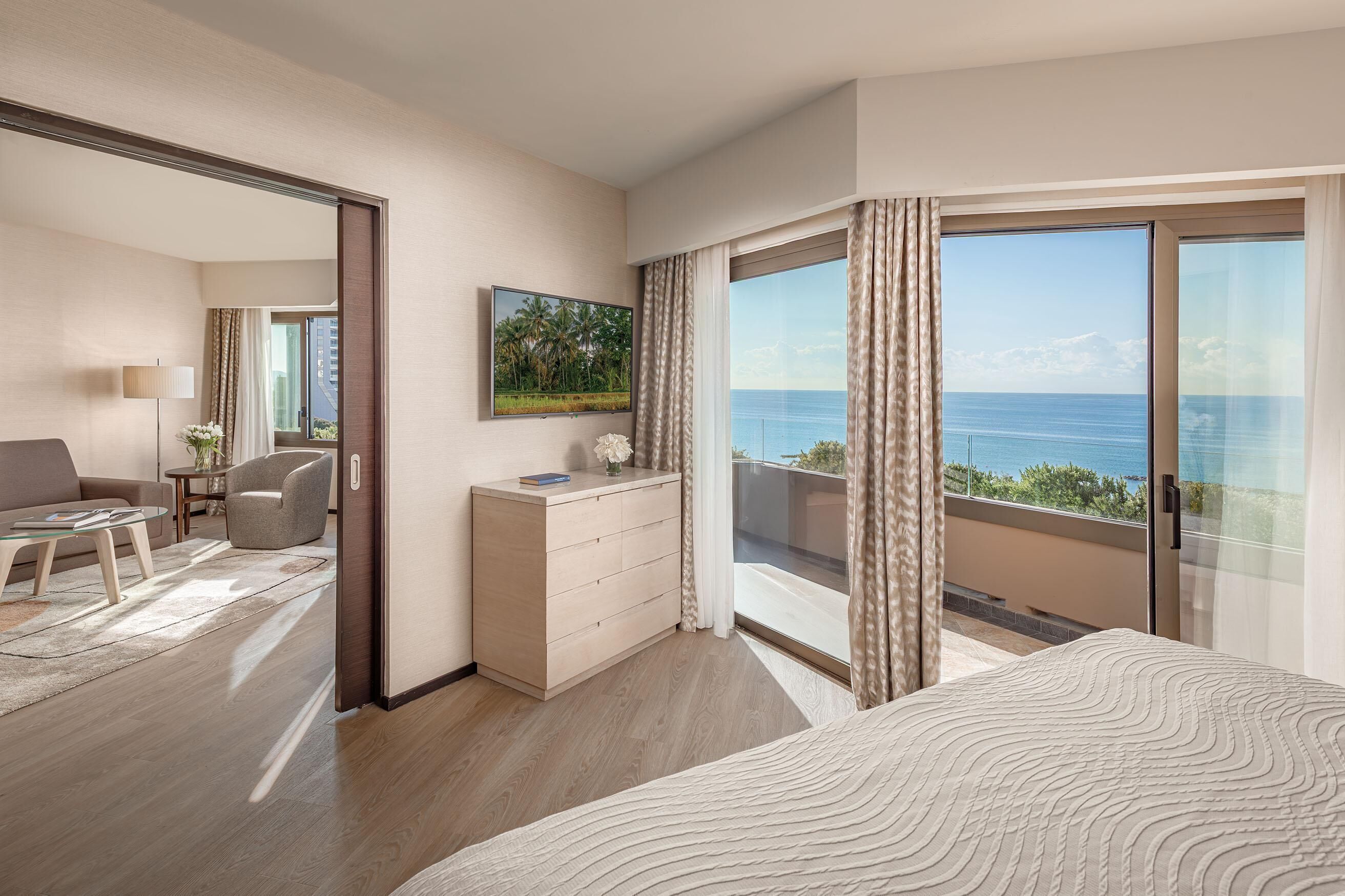 A hotel room with a large bed, a desk, a chair, and a view of the sea.