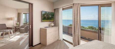 A hotel room with a large bed, a desk, a chair, and a view of the sea.