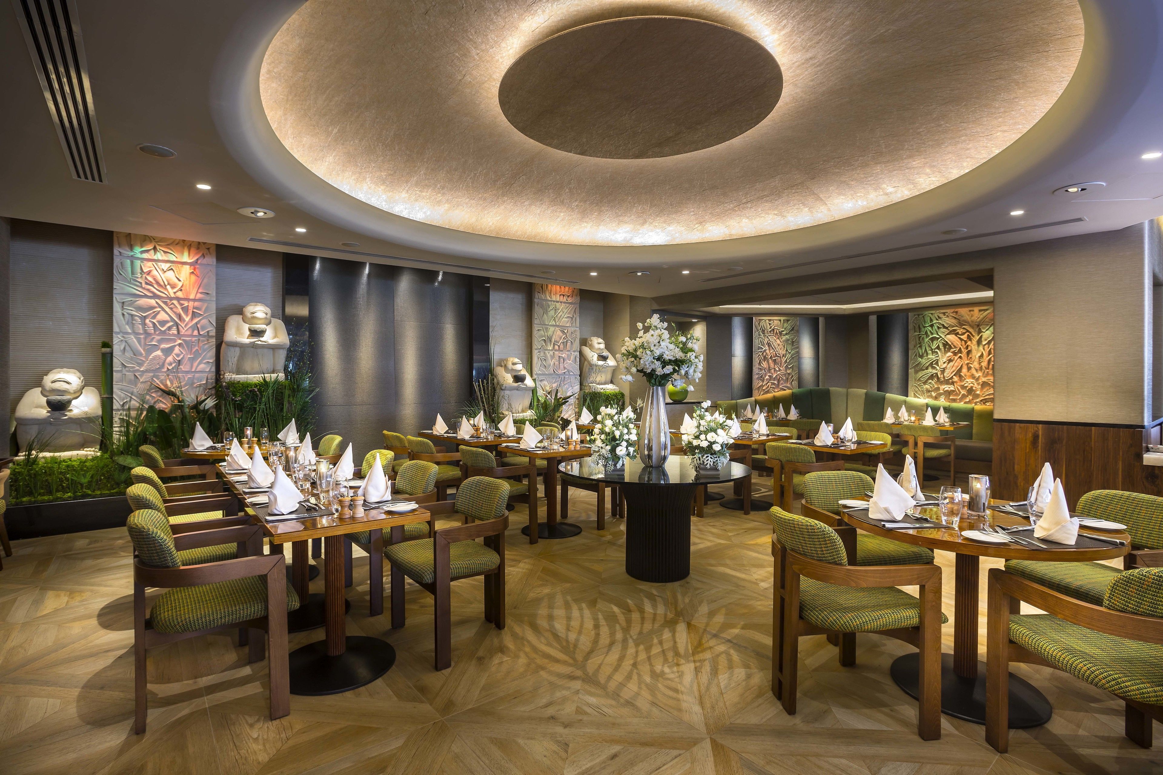 A modern dining area with round tables, green upholstered chairs, and a central decorative piece.