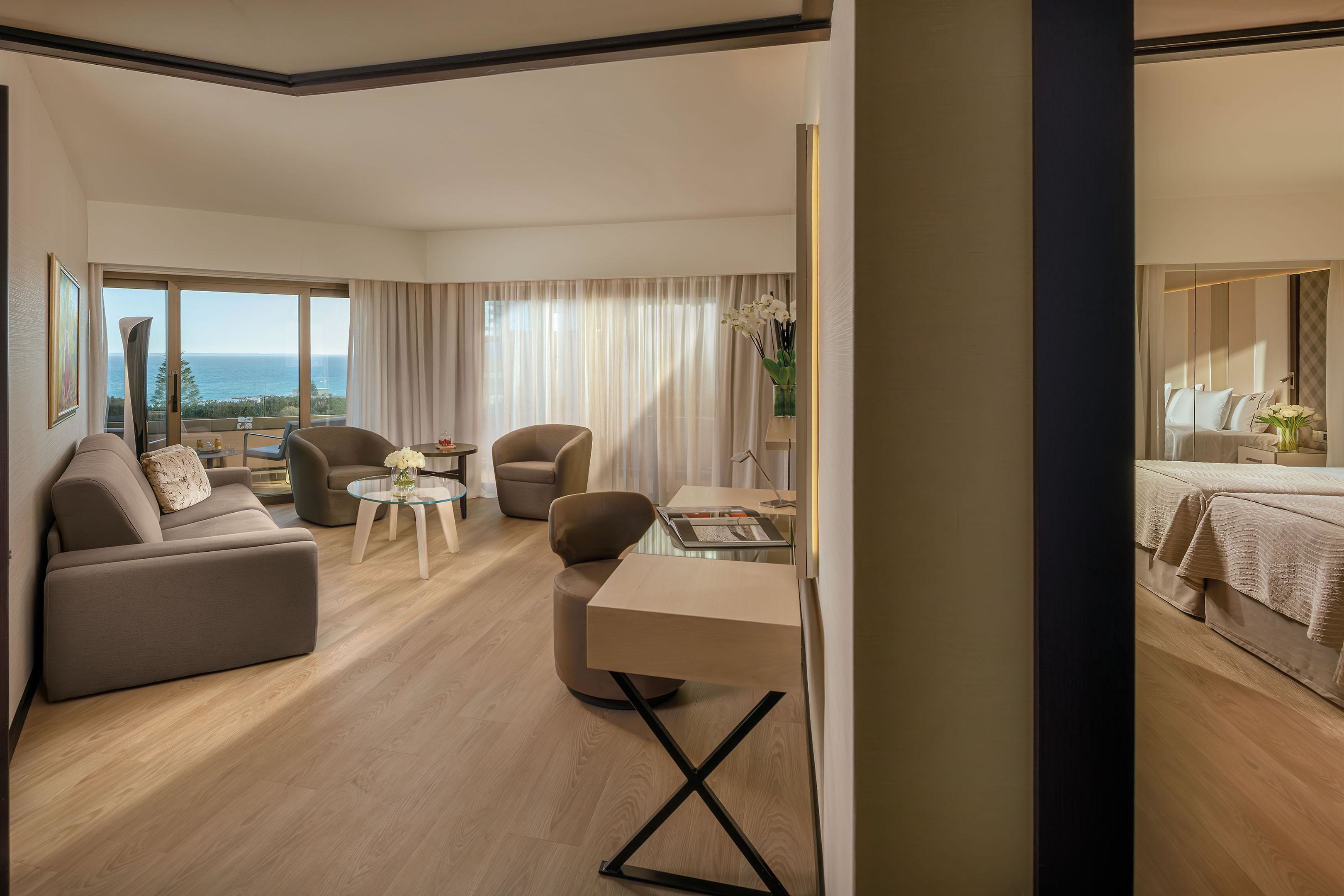 A modern hotel room with a sofa, armchairs, a small table, and a desk.