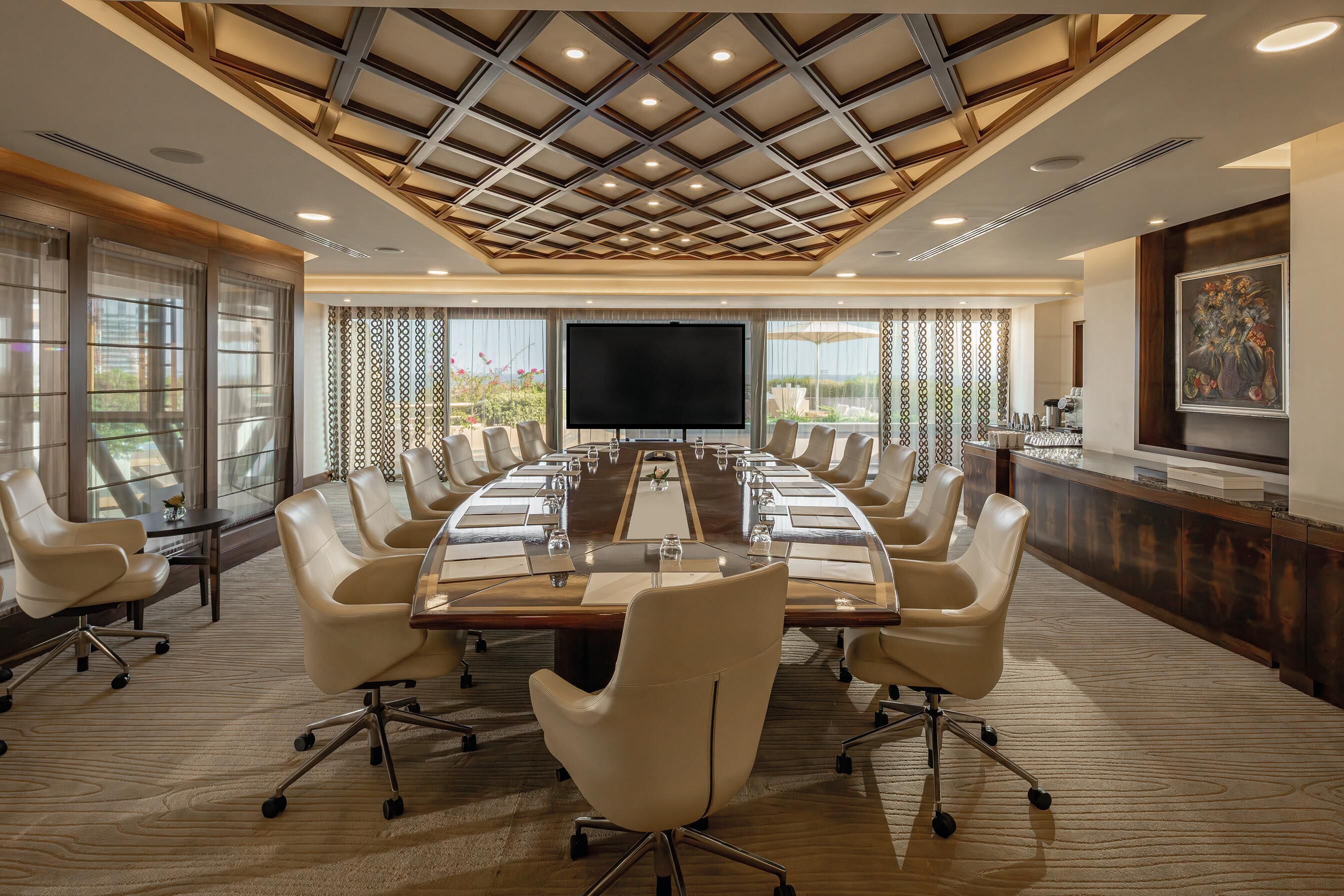 Une salle de conférence dotée d’une longue table, de nombreuses chaises, d’un grand écran et d’un plafond décoratif.