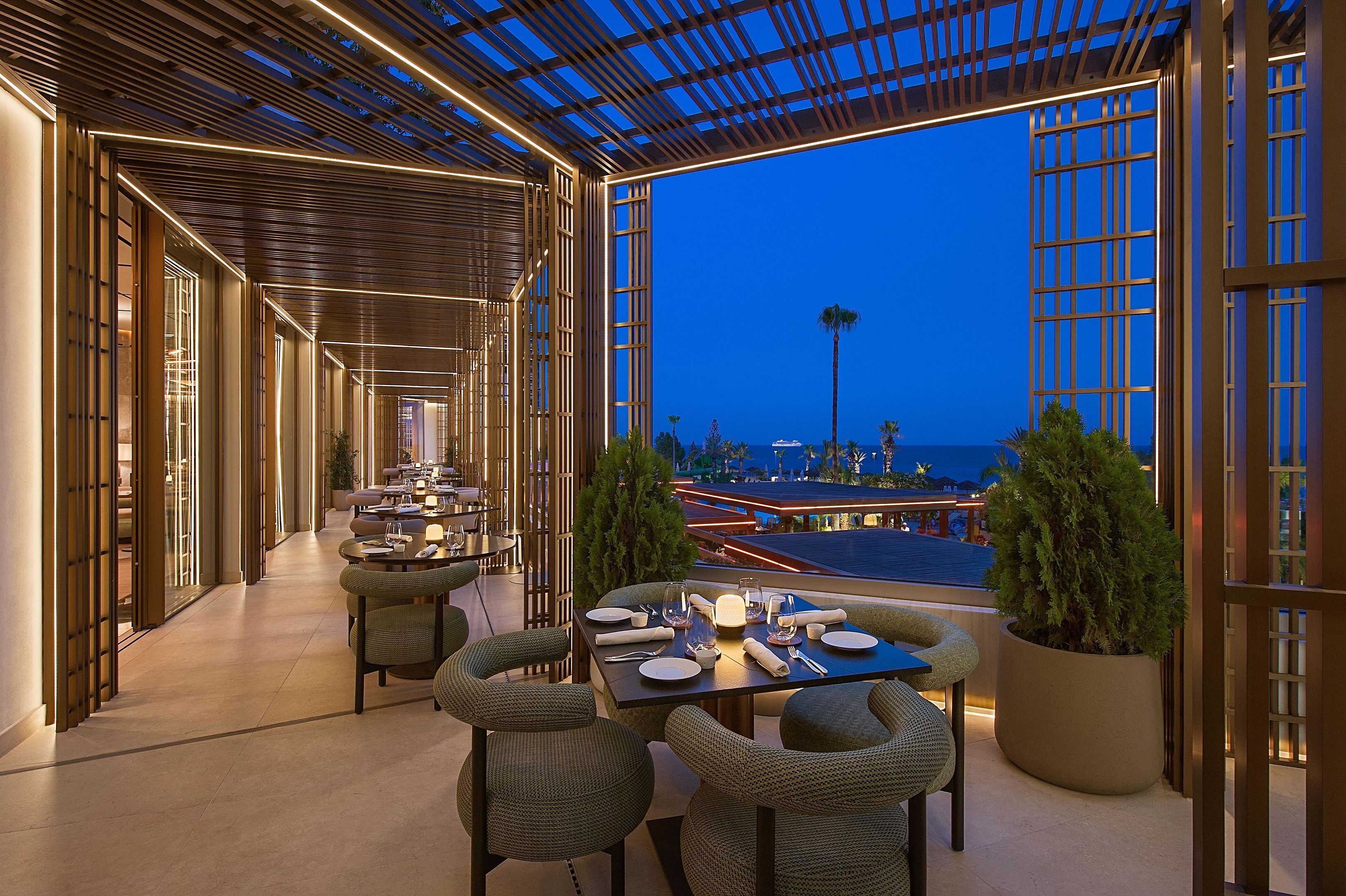 A dining area with a table set for two, a potted plant, and a view of the ocean at dusk.