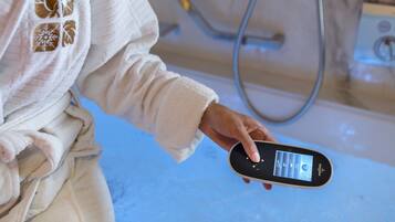 Una persona tiene in mano uno smartphone in un bagno con un pannello di controllo della doccia a vista e un tubo dell'acqua.