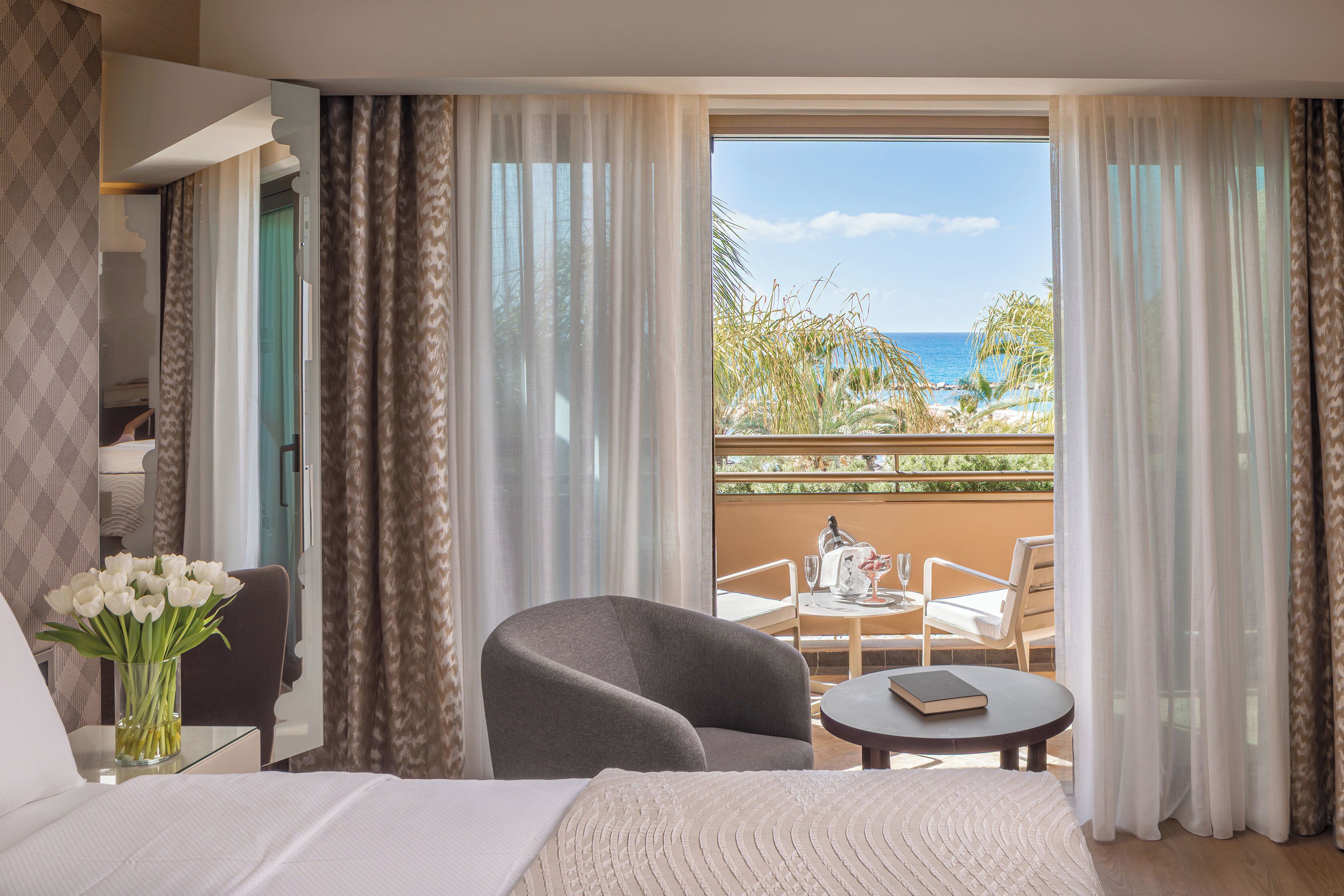 A hotel room with a bed, a chair, a small table, and a view of the ocean.