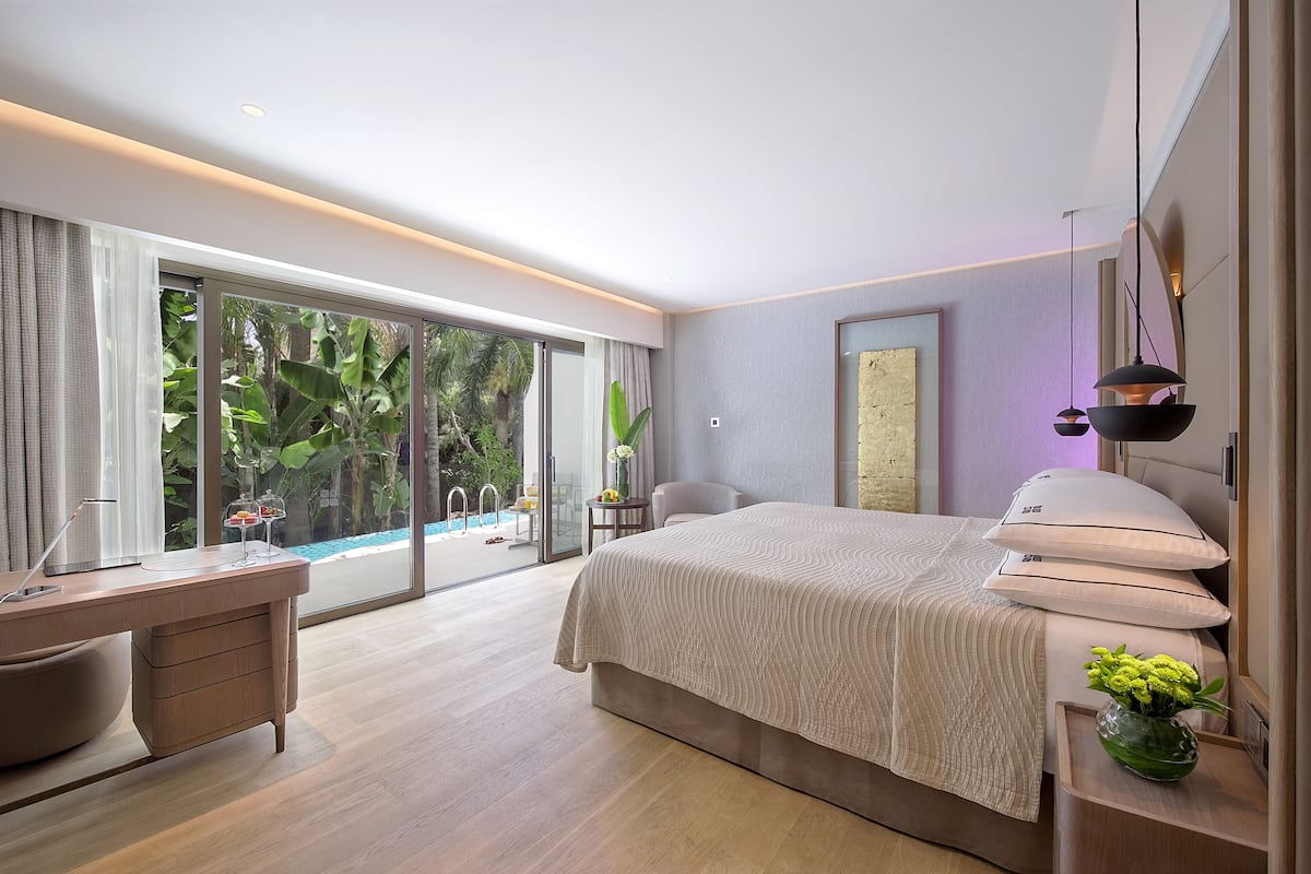 A modern bedroom with a large bed, a desk, and a view of a swimming pool.