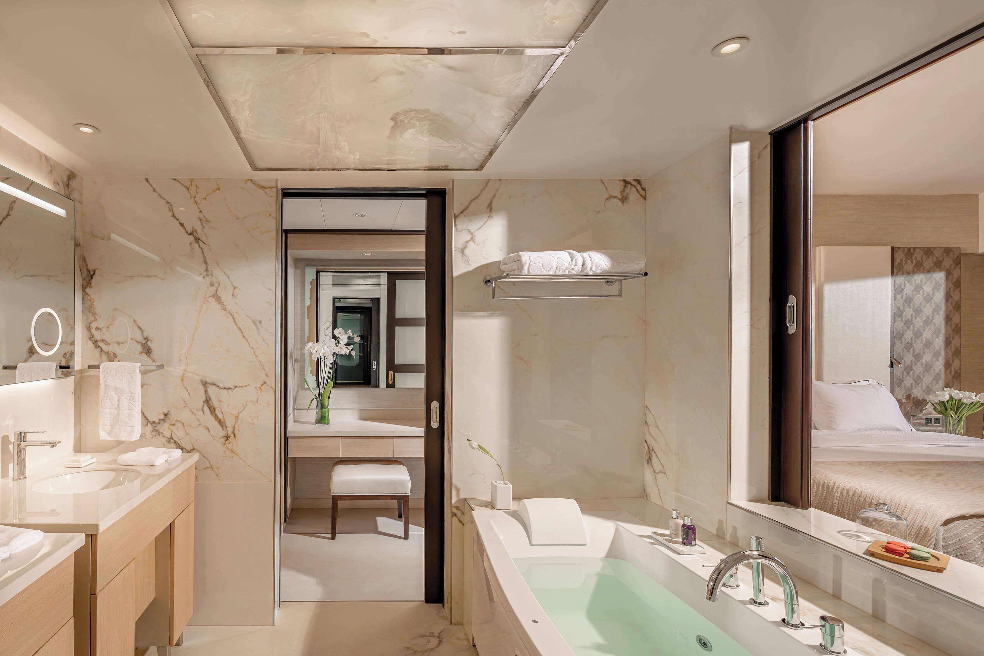 Un baño moderno con salpicadero de mármol, un espejo grande, una bañera y un mueble de tocador con lavabo y toallero.