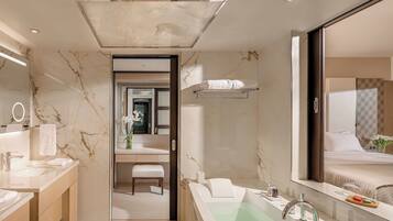 Un baño moderno con salpicadero de mármol, un espejo grande, una bañera y un mueble de tocador con lavabo y toallero.