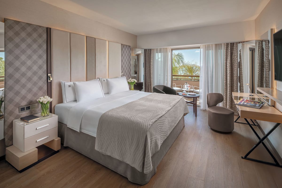 A modern hotel room with a large bed, bedside tables, a desk, and a balcony with a view.