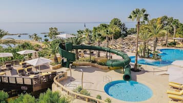 A resort with a water slide, pool, and lounge area with umbrellas.