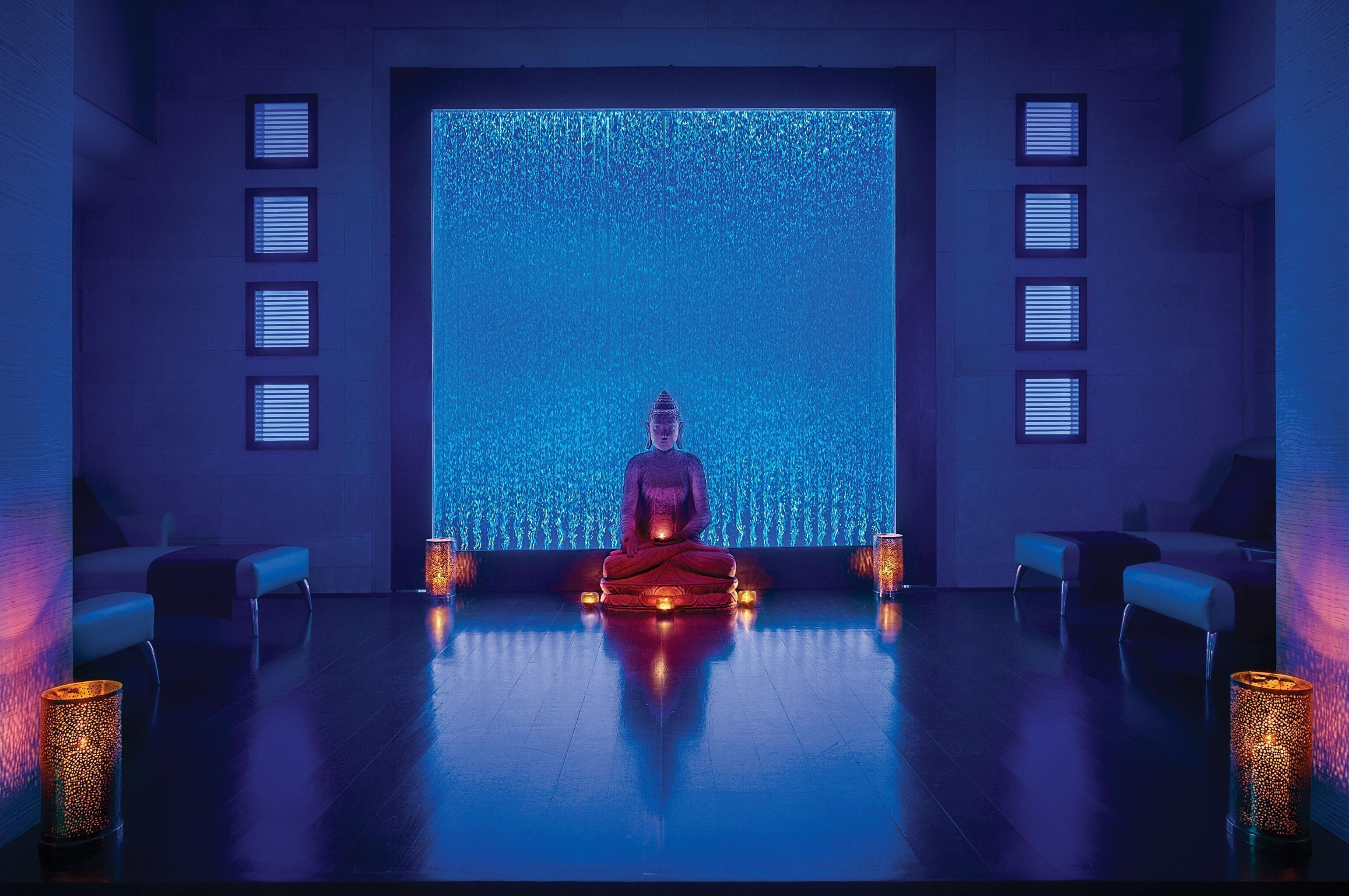 A meditation room with a central figure, a large illuminated wall, and seating on either side.