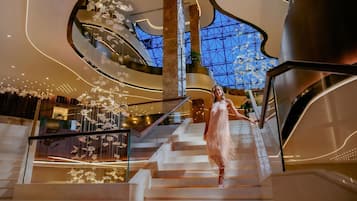 Un interior moderno con una imponente escalera, barandillas de cristal y elementos decorativos colgantes.