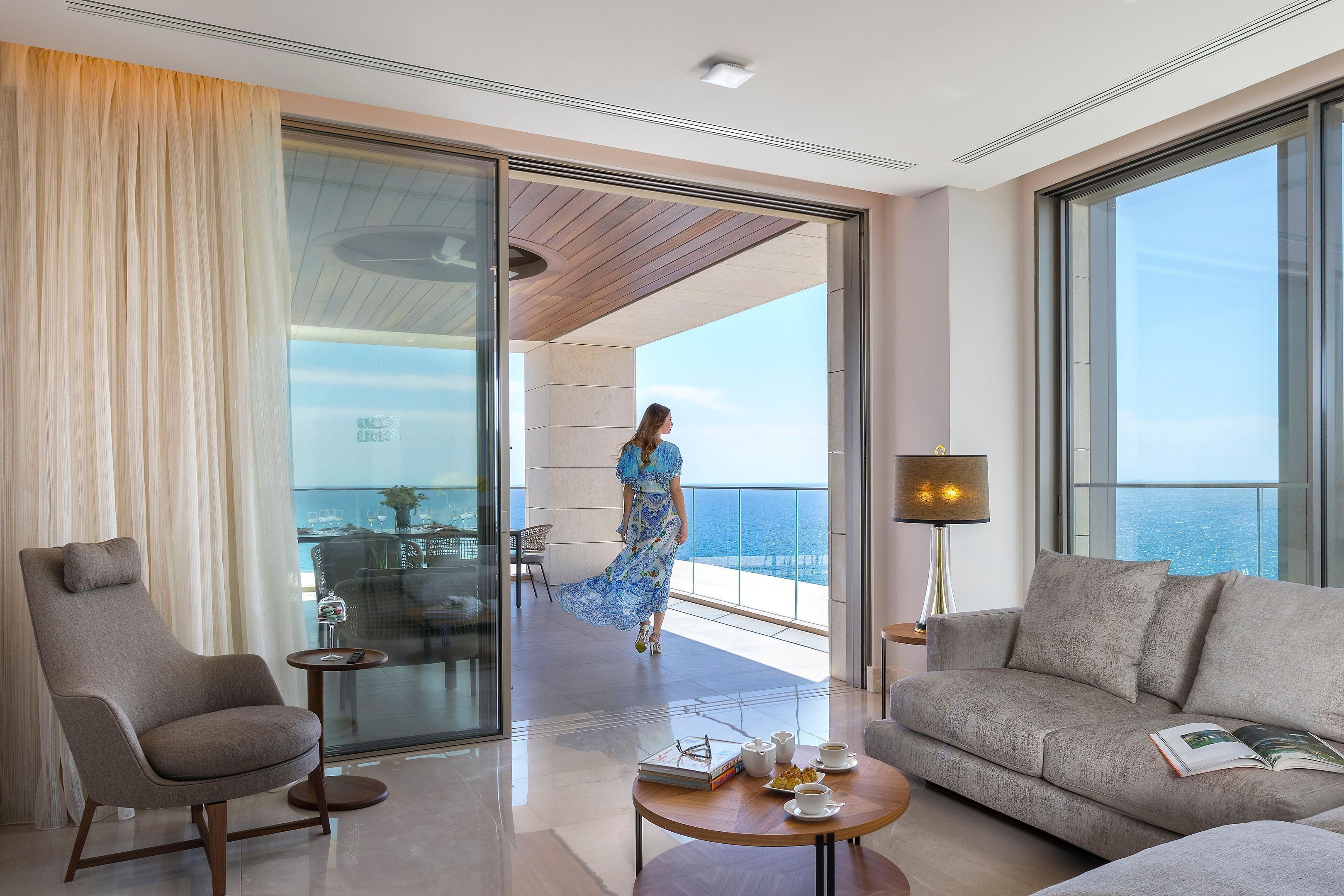 Habitación de hotel moderna con balcón, sofá, sillón, una mesita de centro y vistas al mar.