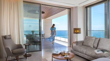 Habitación de hotel moderna con balcón, sofá, sillón, una mesita de centro y vistas al mar.