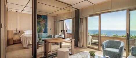 A modern hotel room with a large balcony, a bed, a sitting area, and a dining table.