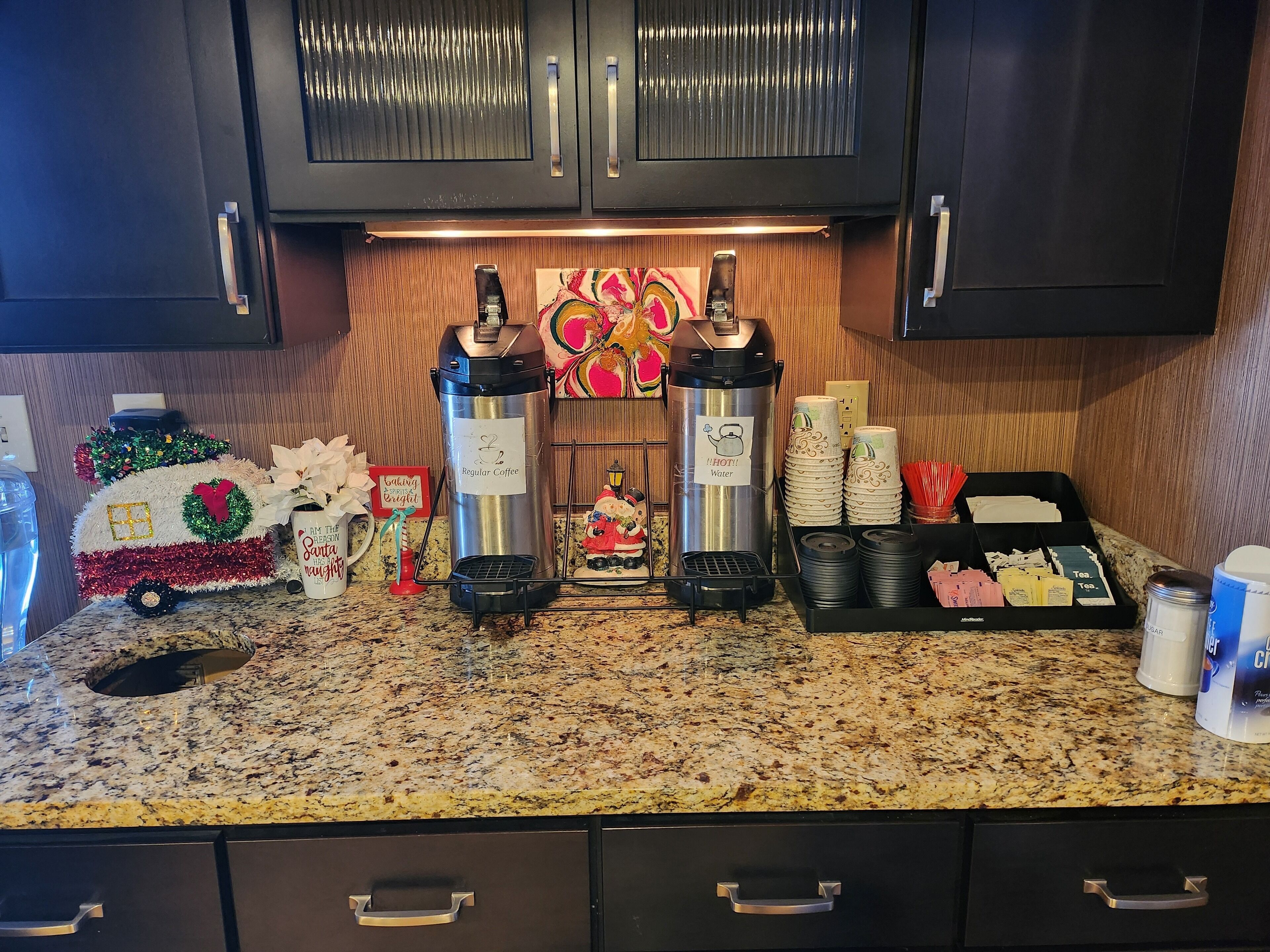 A kitchen counter with coffee makers, a decorative Christmas tree, and holiday-themed items.
