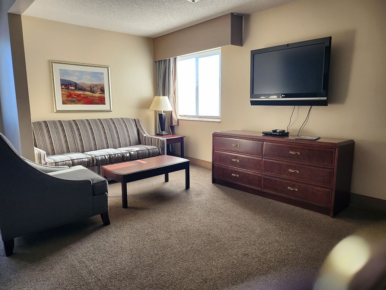 Una sala de estar con sofá, sillón, mesa de centro, televisor y cómoda.