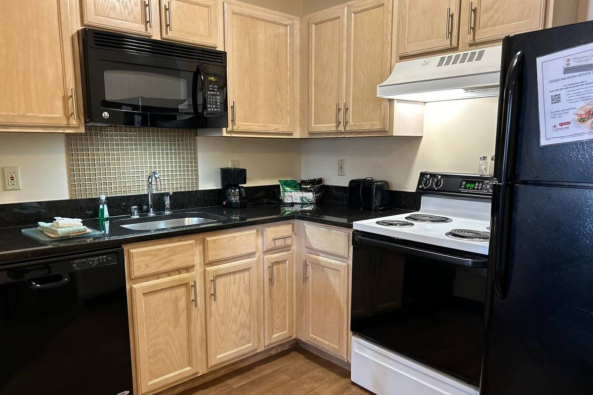A kitchen with wooden cabinets, a black microwave, a white stove, and a black refrigerator.