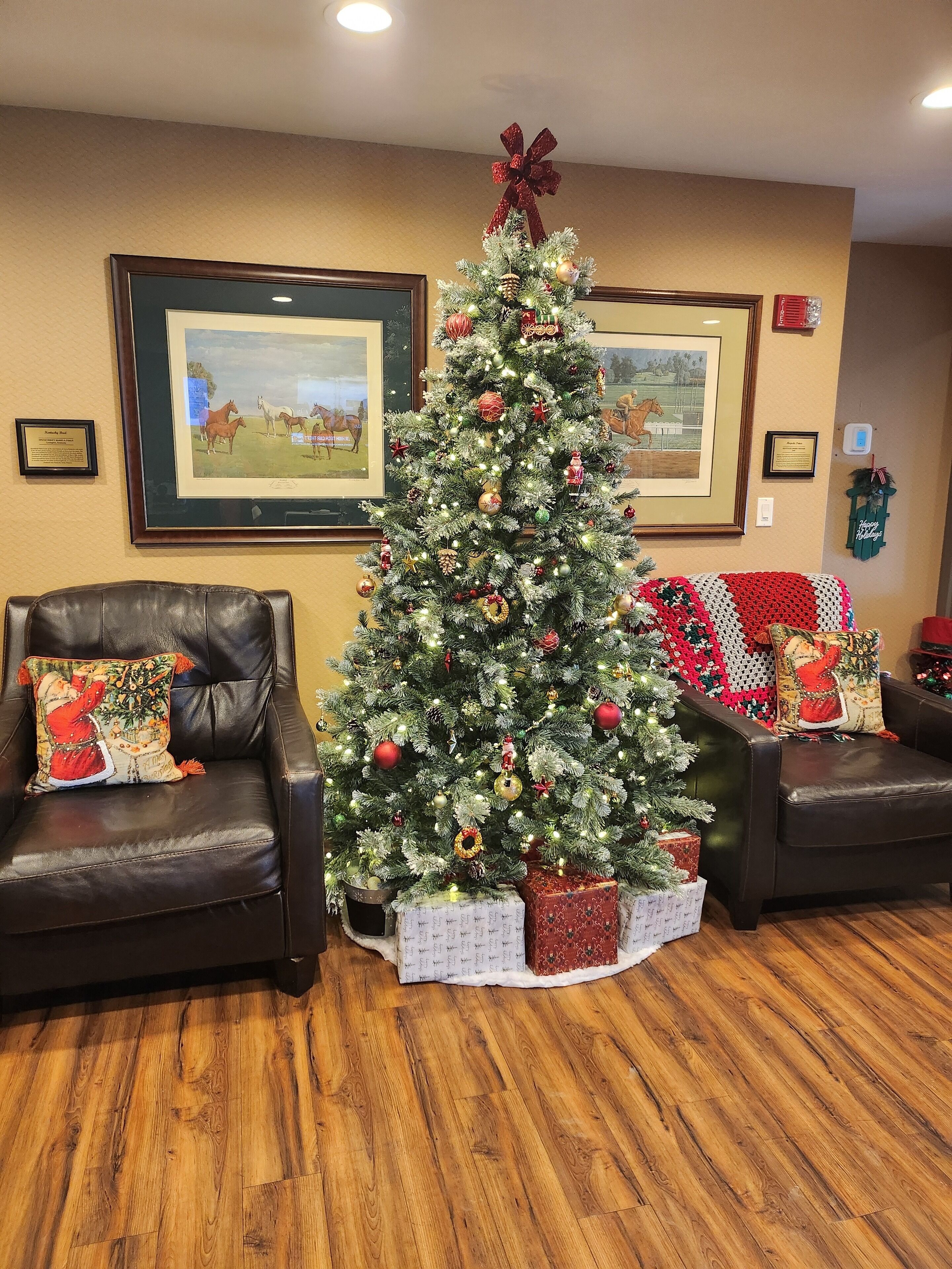 Un salon décoré avec un sapin de Noël, des canapés en cuir, des œuvres d’art encadrées accrochées aux murs et un parquet en bois.
