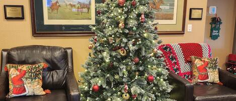 Un salon décoré avec un sapin de Noël, des canapés en cuir, des œuvres d’art encadrées accrochées aux murs et un parquet en bois.