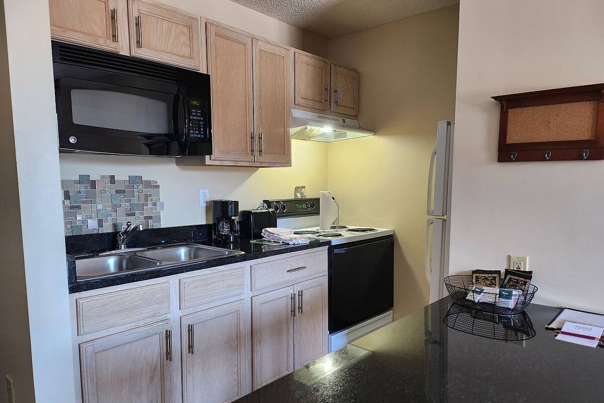 A kitchen with wooden cabinets, a black microwave, a stove, and a refrigerator.