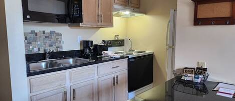 A kitchen with wooden cabinets, a black microwave, a stove, and a refrigerator.