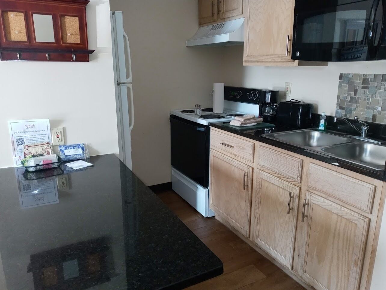 A compact kitchen with a black countertop, a stove, a microwave, and wooden cabinets.