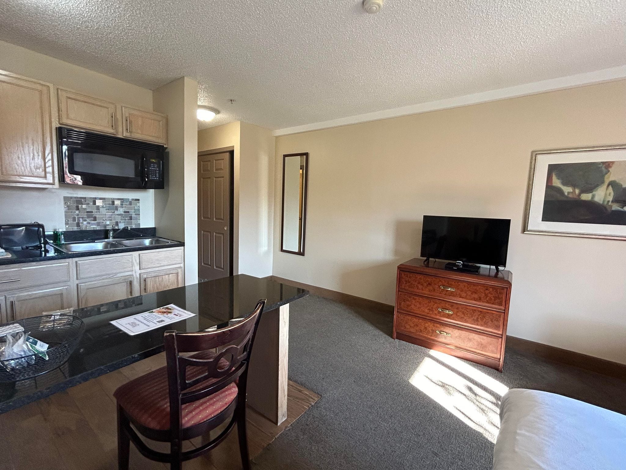 A compact kitchen with a microwave, stove, and sink. There's a dining area with a table and chairs, and a TV on a dresser.