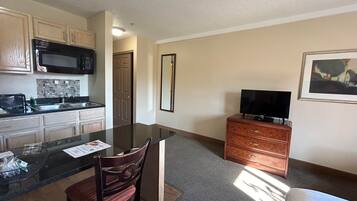 A compact kitchen with a microwave, stove, and sink. There's a dining area with a table and chairs, and a TV on a dresser.