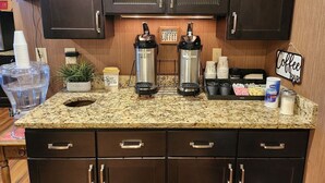 Una cocina con armarios oscuros, encimera de granito y dos cafeteras. Hay tazas de café, un letrero que dice ‘Coffee Bar’ y una planta en la encimera.