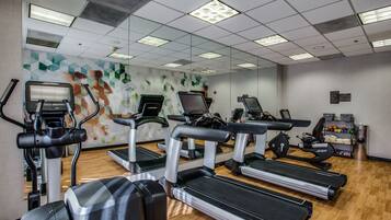 A gym with treadmills, ellipticals, and a mirrored wall.