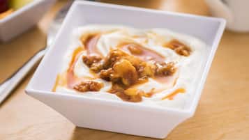 Un tazón blanco de yogur cubierto de nueces y jarabe sobre una mesa de madera.