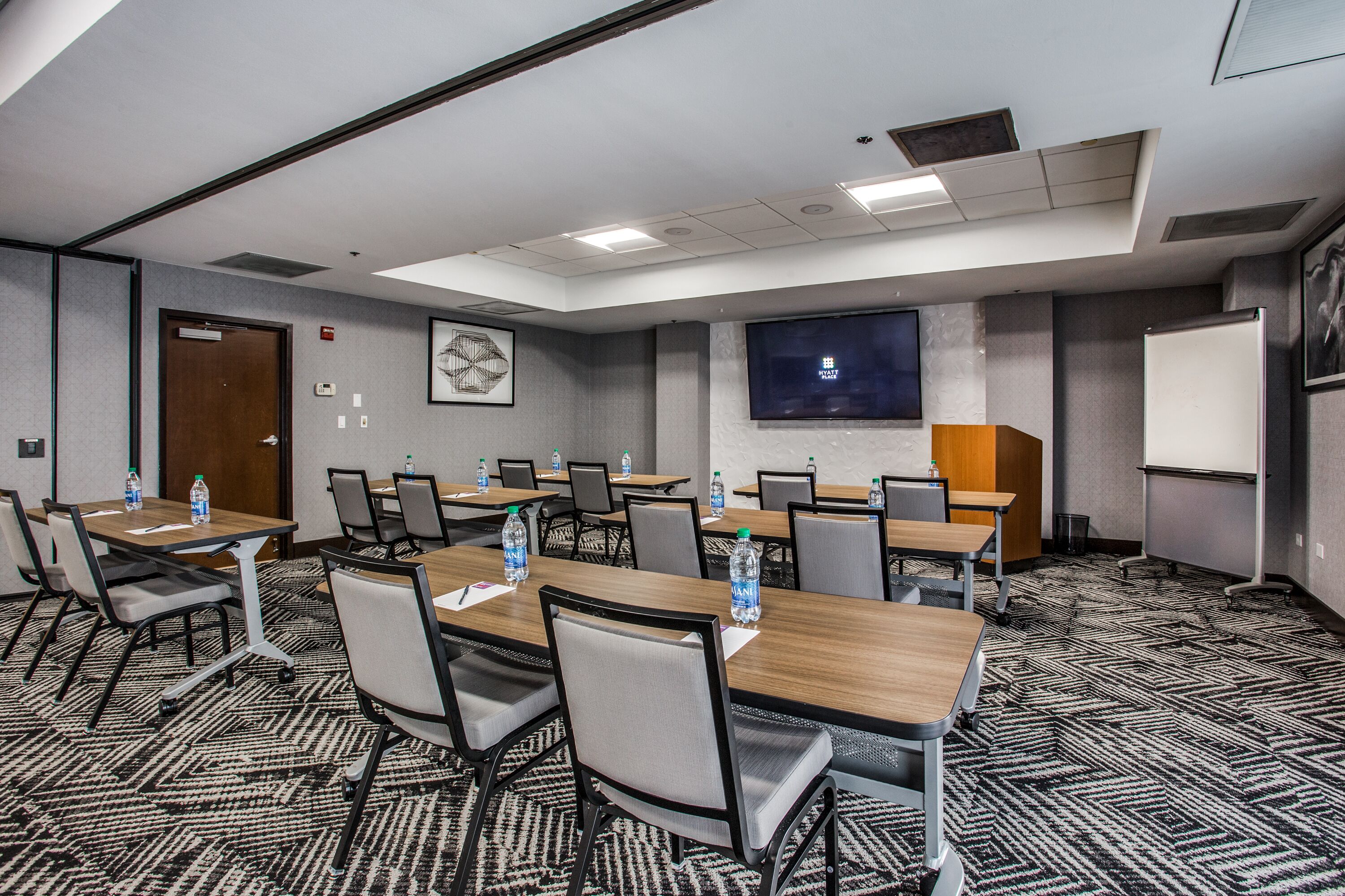 A conference room with multiple tables, chairs, and a large screen.