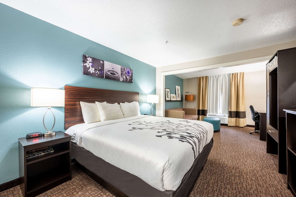 A hotel room with a large bed, a nightstand with a clock, a desk, and a chair.