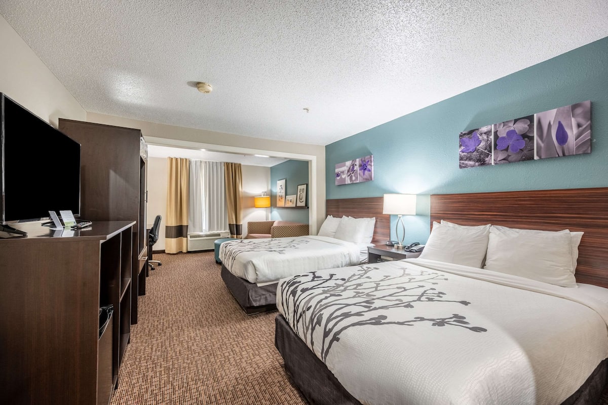 A hotel room with two beds, a desk with a TV, and artwork on the walls.