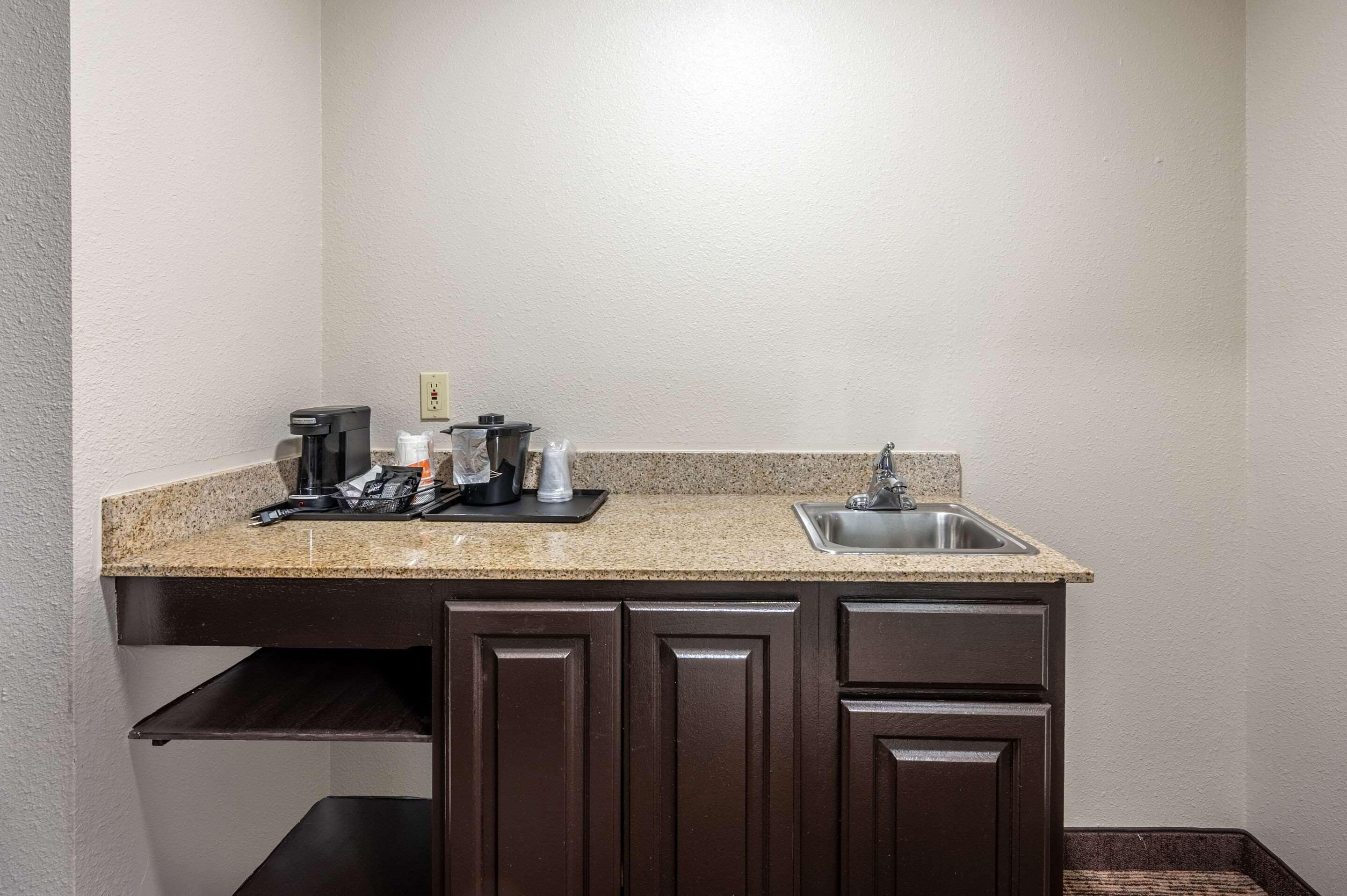 A small kitchen with a granite countertop, dark wooden cabinets, a stainless steel sink, and a coffee maker.