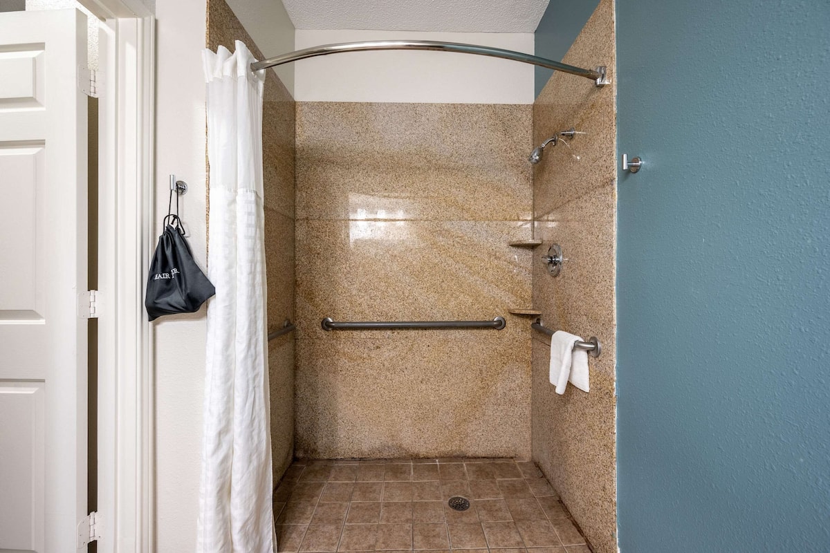 A bathroom with a shower, a towel rack, and a handrail.