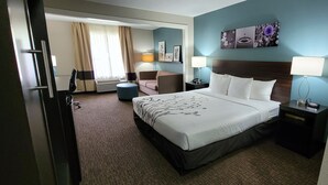 A hotel room with a large bed, a bedside table, a chair, a small table, a lamp, and a window with curtains. - Sleep Inn & Suites Birmingham - Hoover (Birmingham)