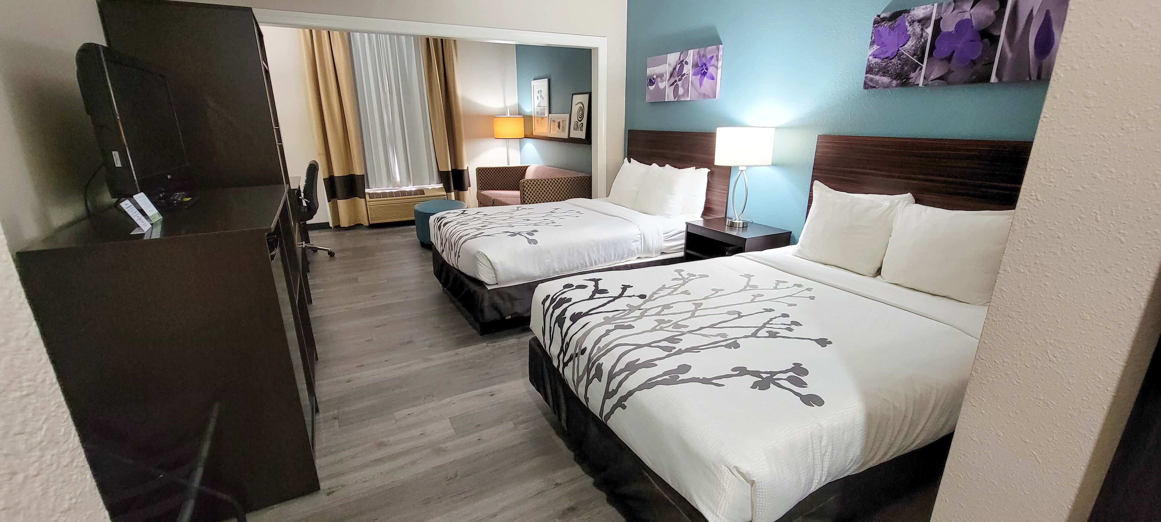 A hotel room with two beds, a desk, a chair, a TV, and a window with curtains.