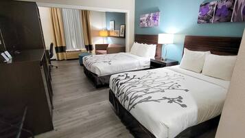 A hotel room with two beds, a desk, a chair, a TV, and a window with curtains.
