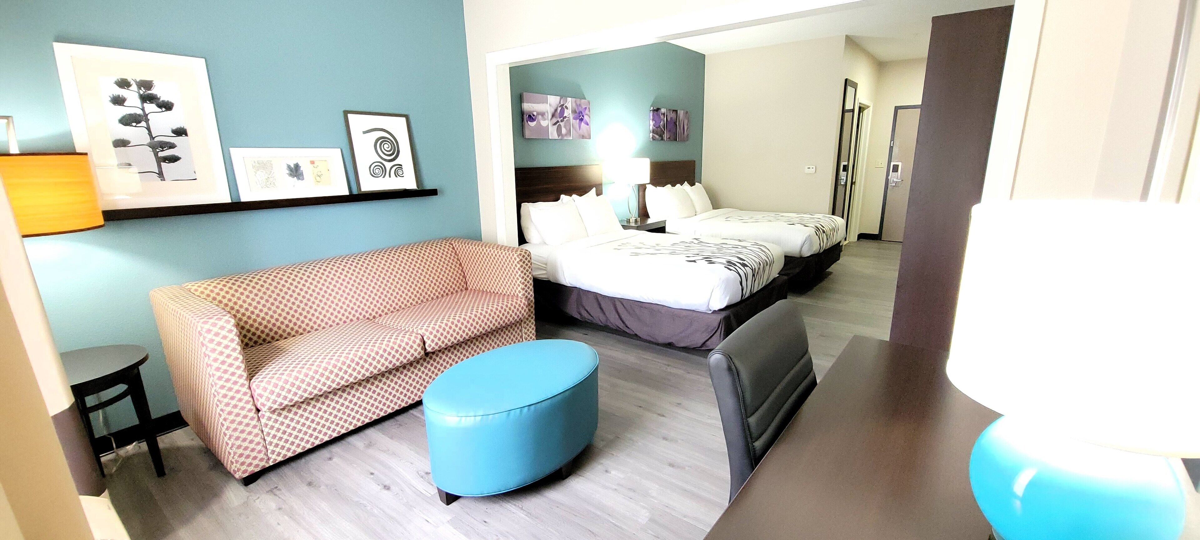 A hotel room with a sofa, ottoman, and a bed with a headboard.