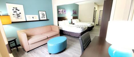 A hotel room with a sofa, ottoman, and a bed with a headboard.