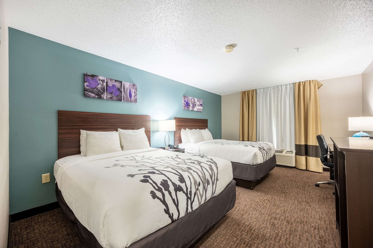 A hotel room with two beds, a desk, a chair, and a window with curtains.