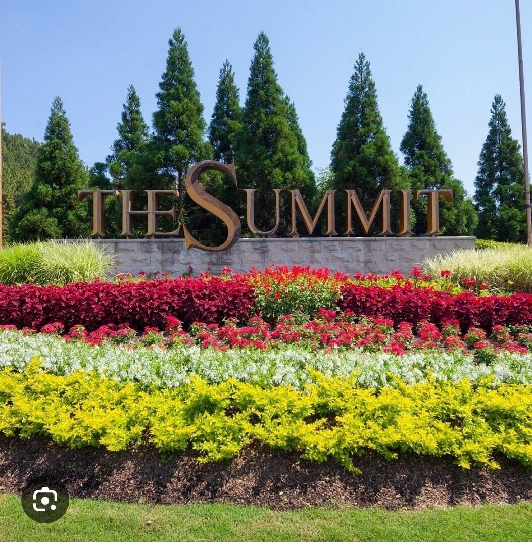 Een bord met 'THE SUMMIT' in grote letters, omringd door diverse kleurrijke bloembedden.