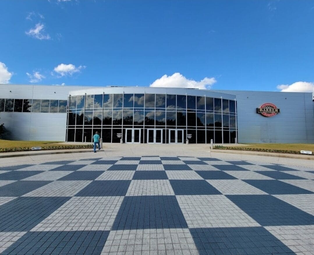 A modern building with a glass facade and a checkered pavement in front.