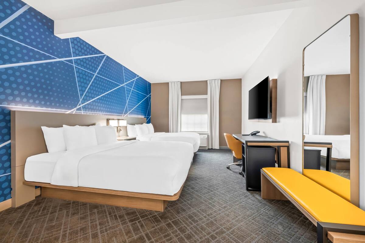 A hotel room with a large bed, a desk, a chair, a TV, and a mirror.