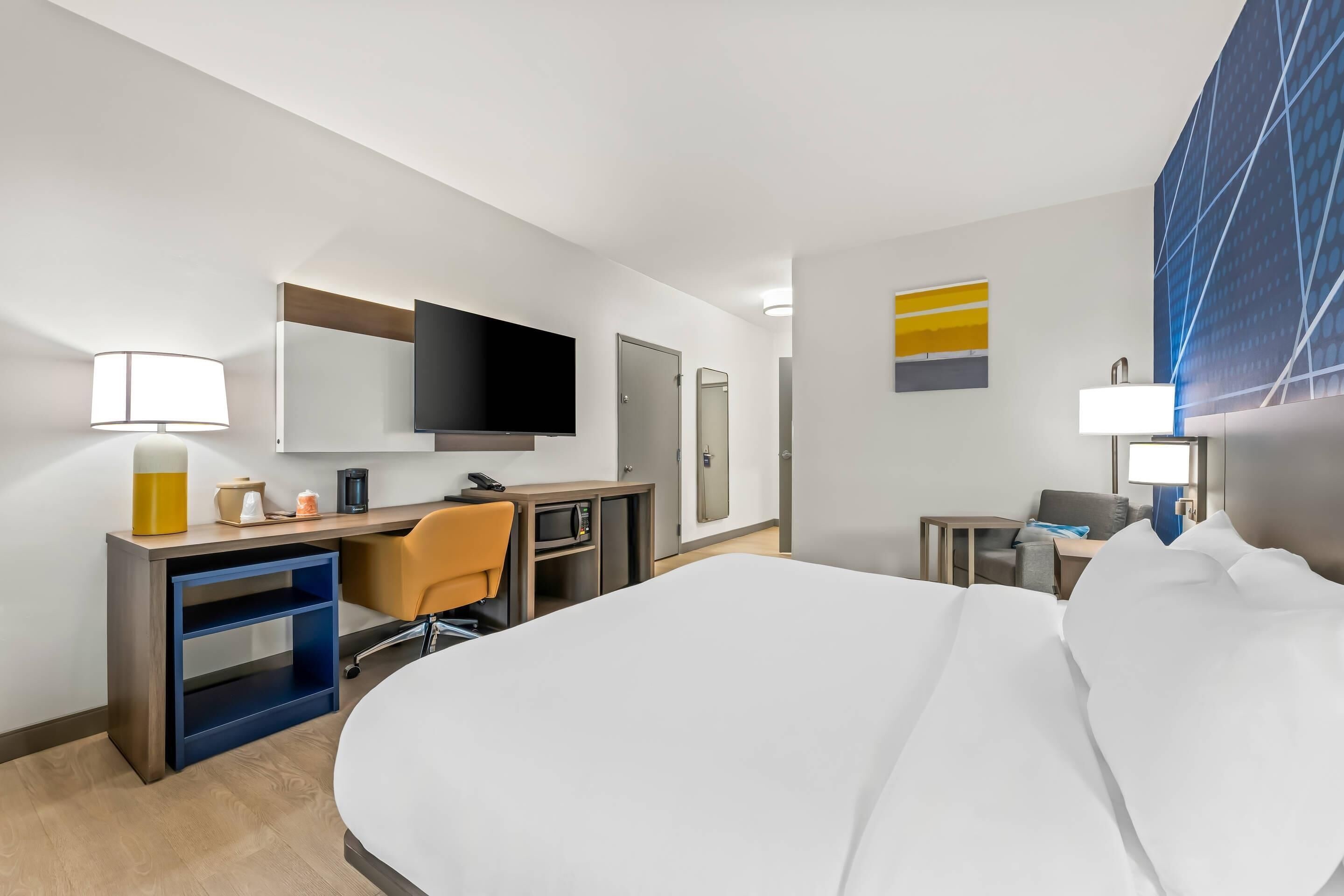 Una camera d'albergo con un letto, una scrivania, una sedia, televisore e un comodino con lampada.